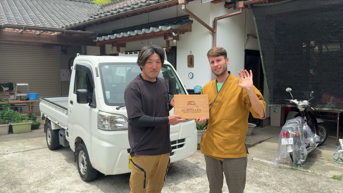 Akio-san of Kurihara Seicha holding an engraved wooden Kurihara nameplate with Christian Mauerer beside him outside the family compound in Yame, Fukuoka