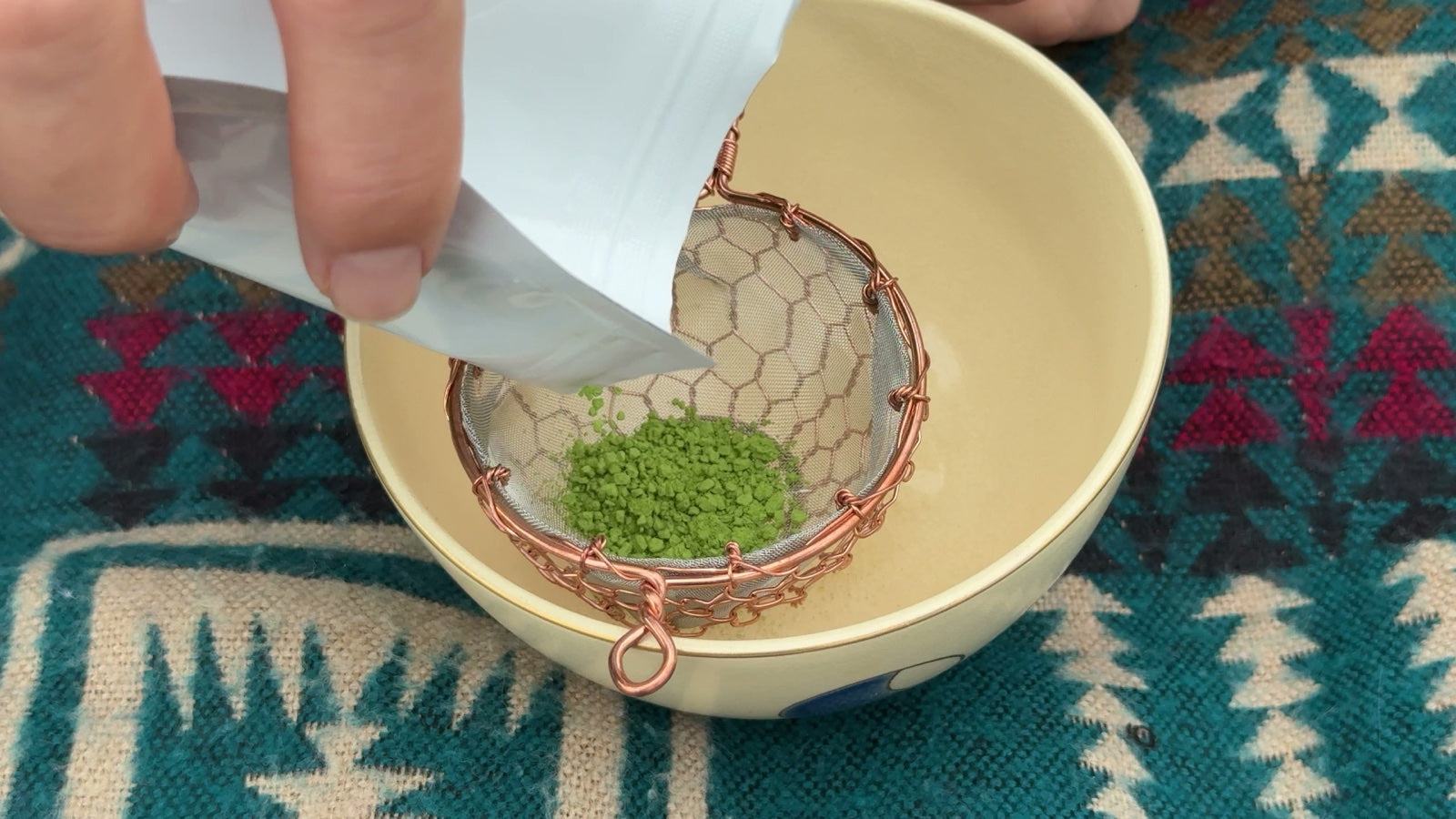 Vivid green matcha powder poured through a copper sieve into a bowl