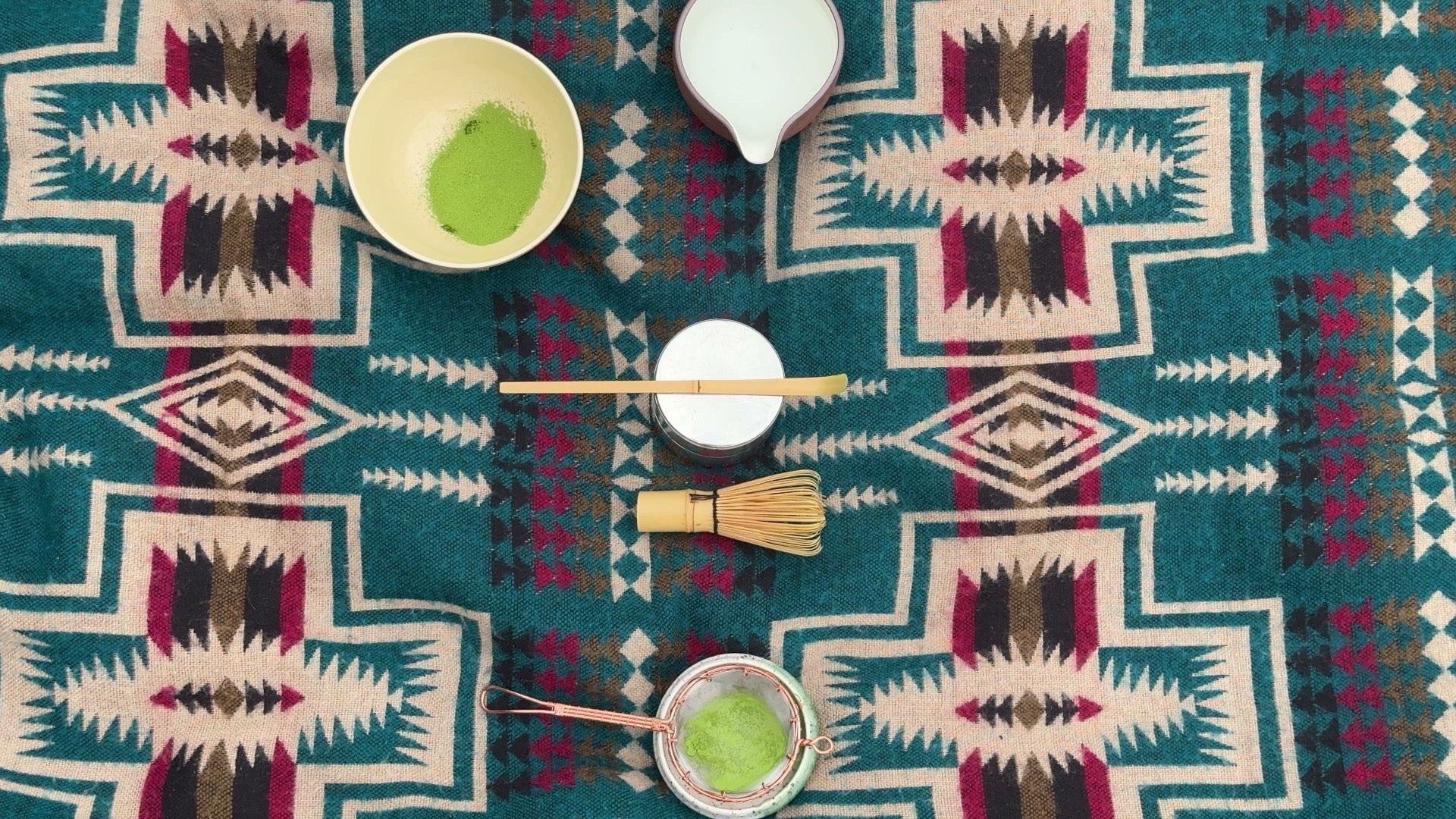 Overhead flat-lay of matcha: a bowl, bamboo whisk and scoop, and sifted green powder