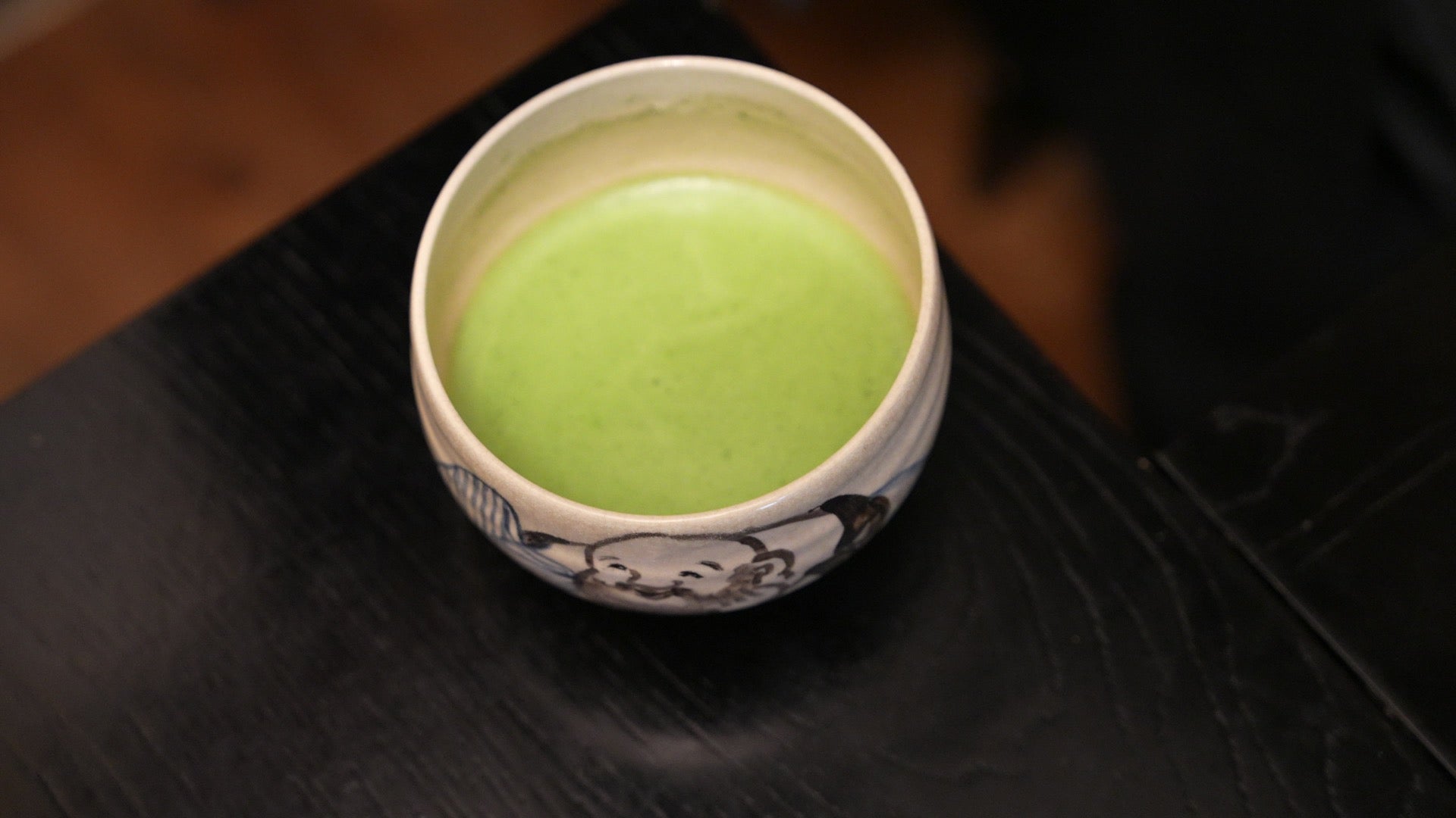 A bowl of freshly whisked bright green matcha on a dark table
