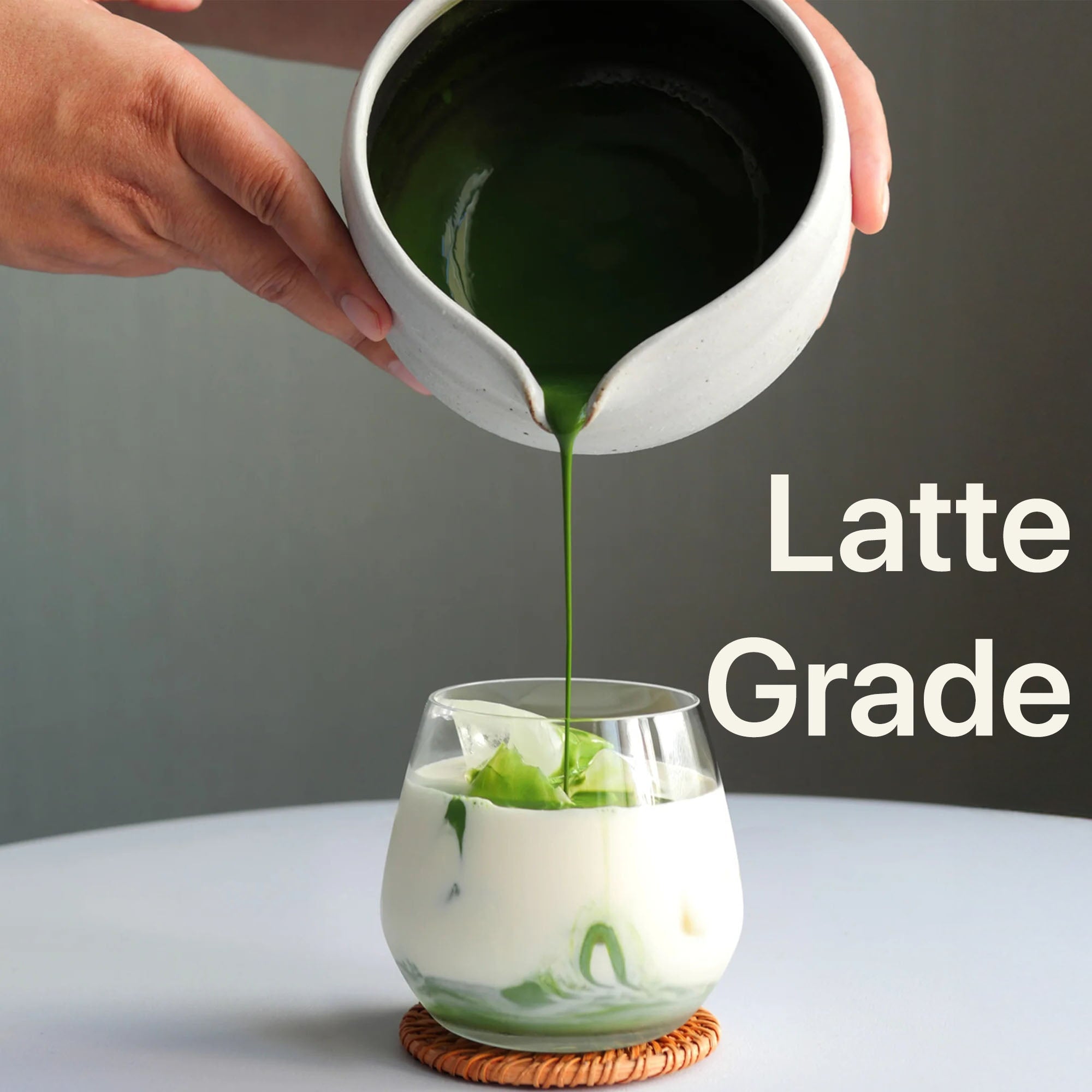 USDA Organic Latte Grade Matcha Powder in a ceramic bowl pouring into a glass with milk and green tea swirls.