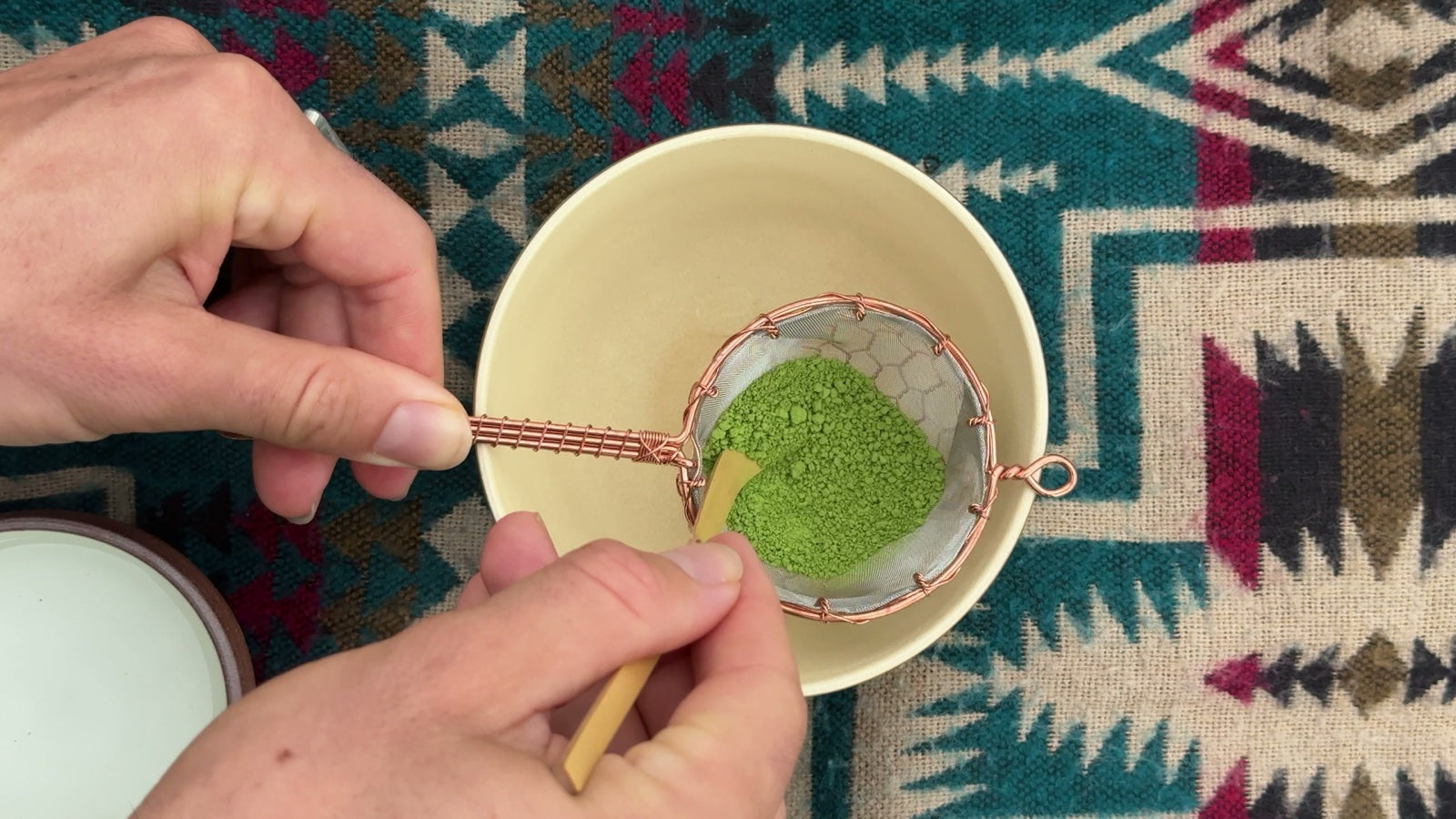 Matcha powder sifted through a copper strainer into a bowl