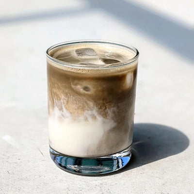 Iced hojicha latte with creamy swirl in a clear glass on a light surface.